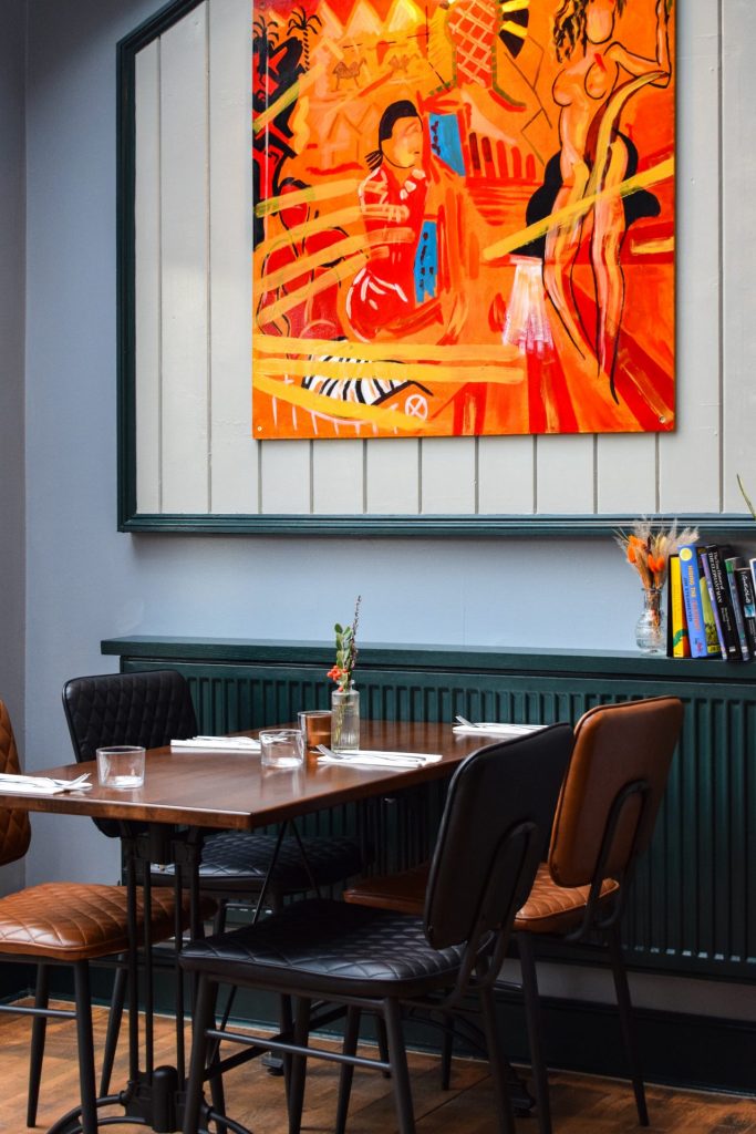 Picture of a table under and red and orange piece of modern artwork at The Lazy Elephant in Sandwich.