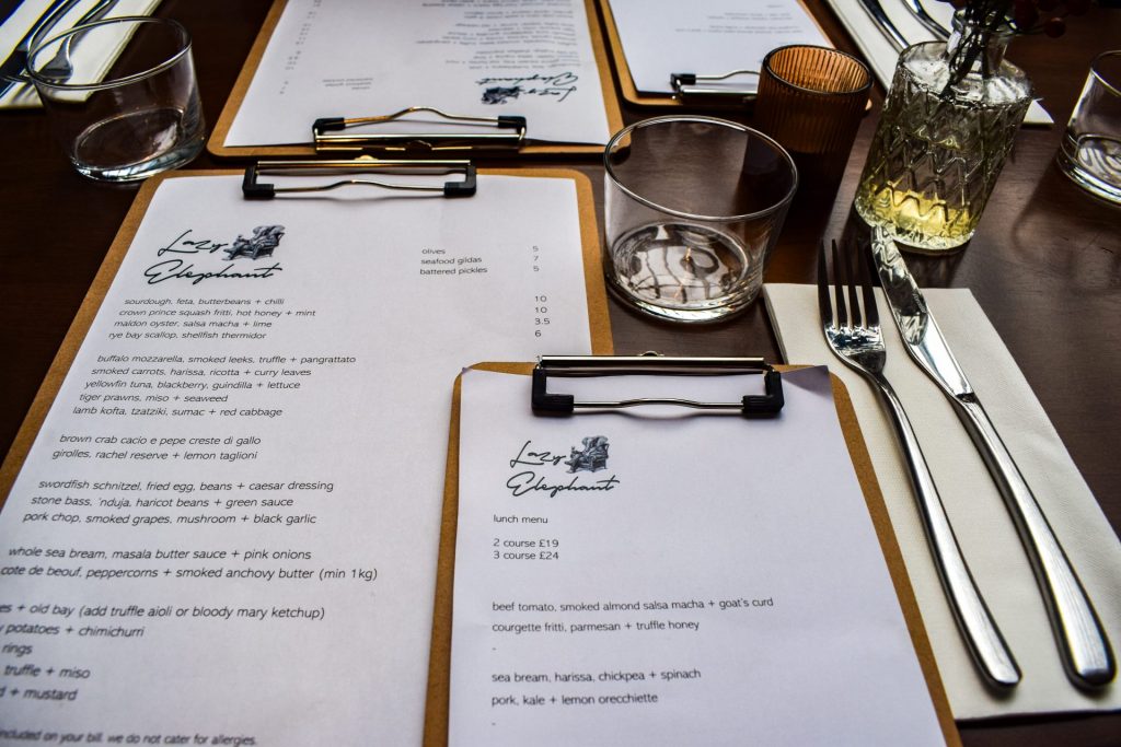 Menus for The Lazy Elephant in Sandwich set on a set table in clipboards.
