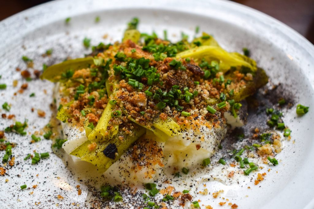 Close up of smoked leeks on top of a torn mozzarella ball, topped with chopped chives and crispy breadcrumbs.