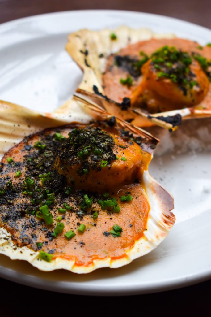 Close up of two scallops thermidor in their shells on a white plate.
