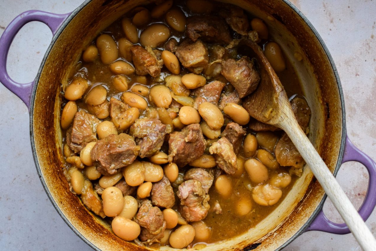 Close up of a purple casserole dish with butter beans and pork.