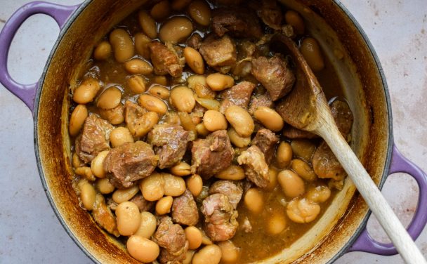 Close up of a purple casserole dish with butter beans and pork.