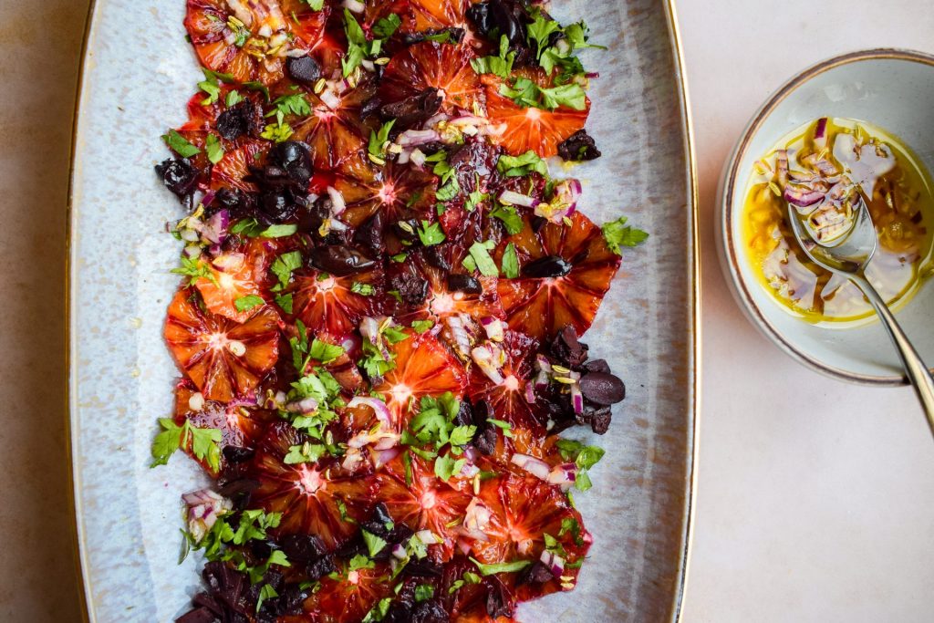 Blood orange and black olive salad with a vibrant bowl of lemon and red onion dressing to one side.