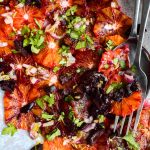 Close up of a fork and spoon sitting in a platter of orange and black olive salad.