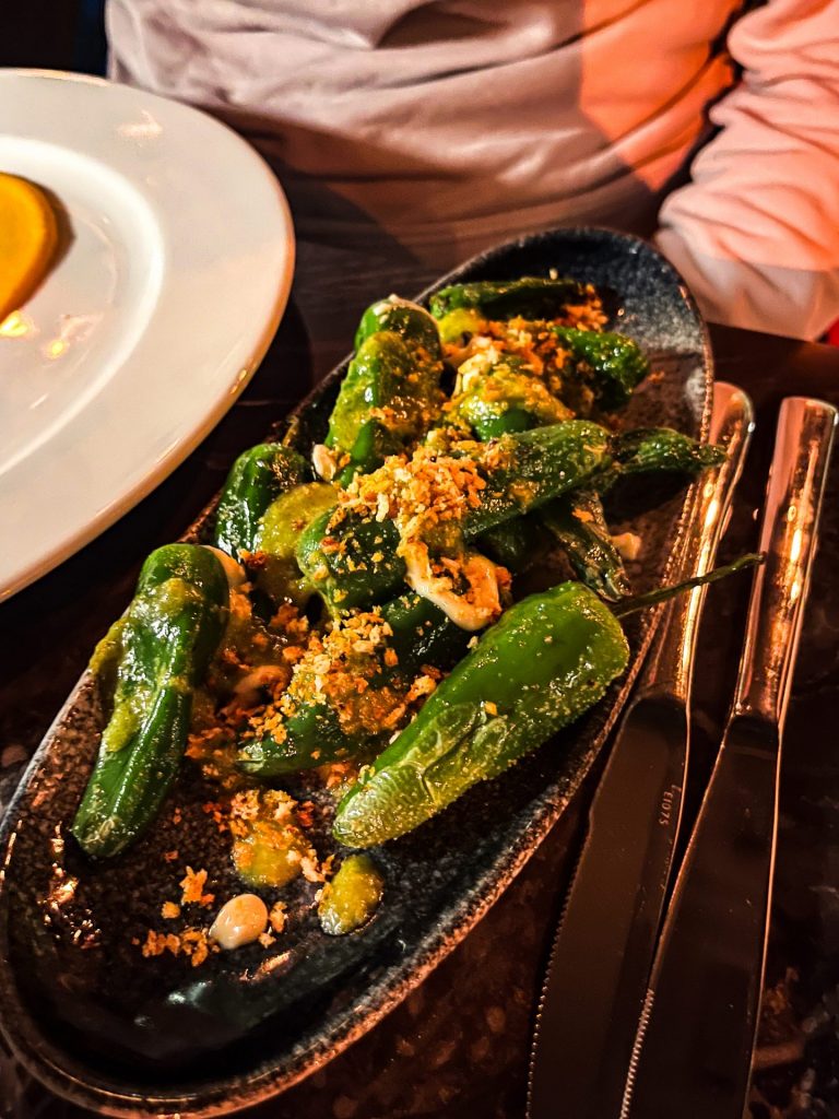 Platter of blistered padron peppers topped with jalapeno sauce. 
