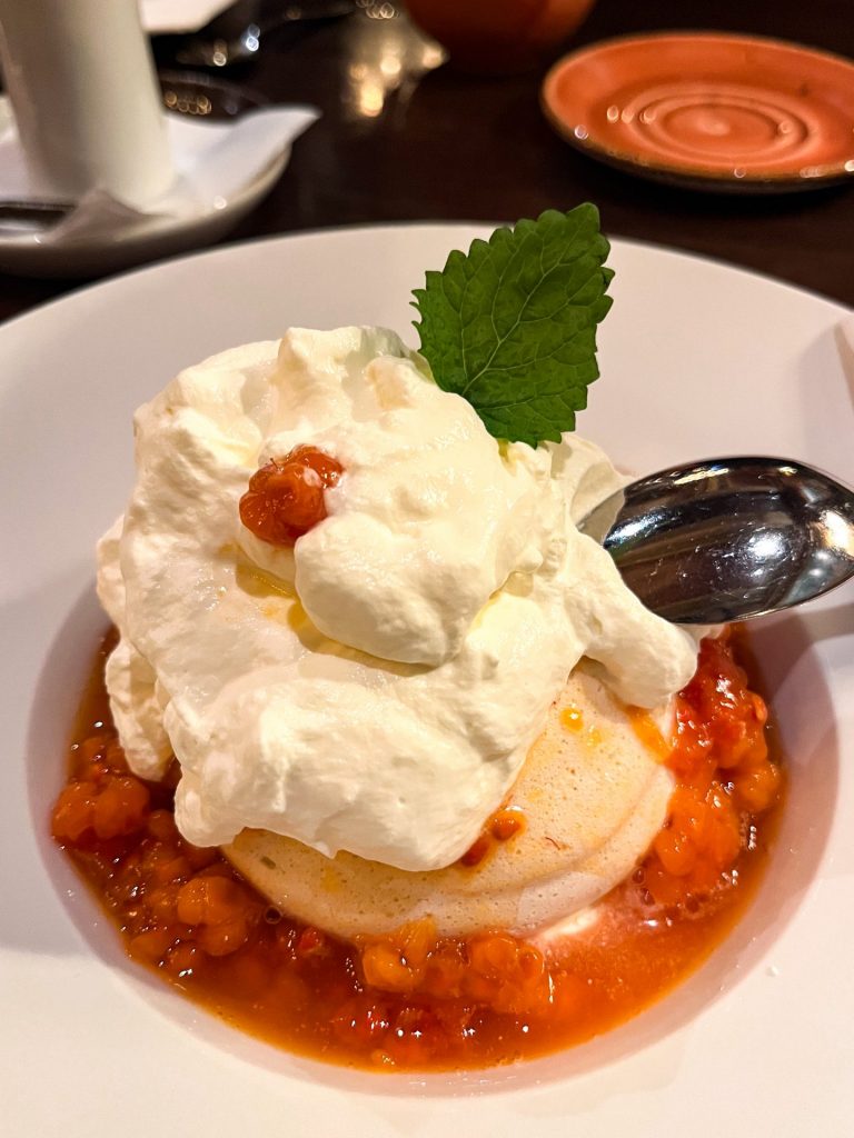 Cloudberry pavlova in a white bowl garnished with a sprig of lemon balm.