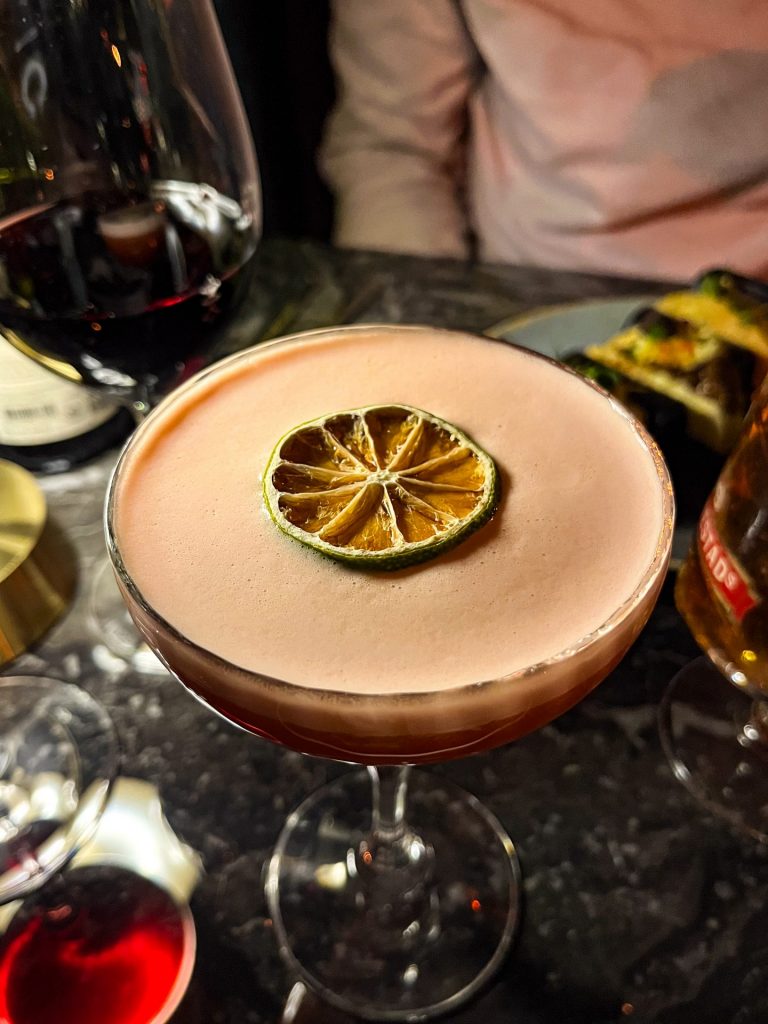 Cocktail topped with foam and a dried lime wheel.