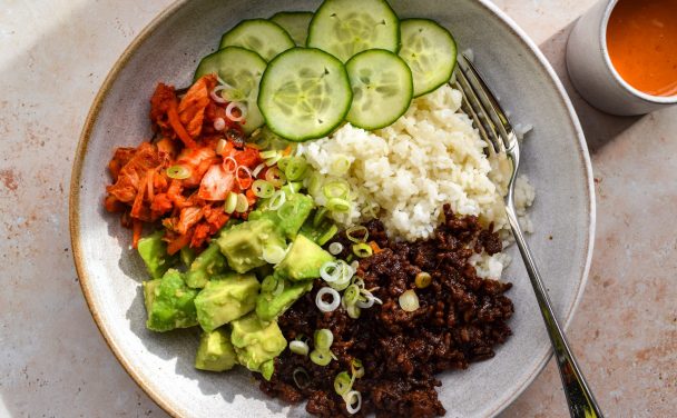 Bowl of korean beef mince, rice, avocado, kimchi and sliced cucumber.