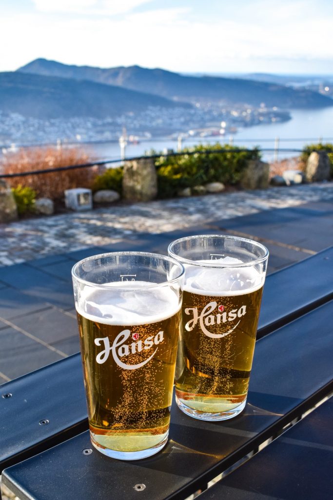 A pair of beers on a table with the view over Bergen from the top of Mount Fløyen in the background.