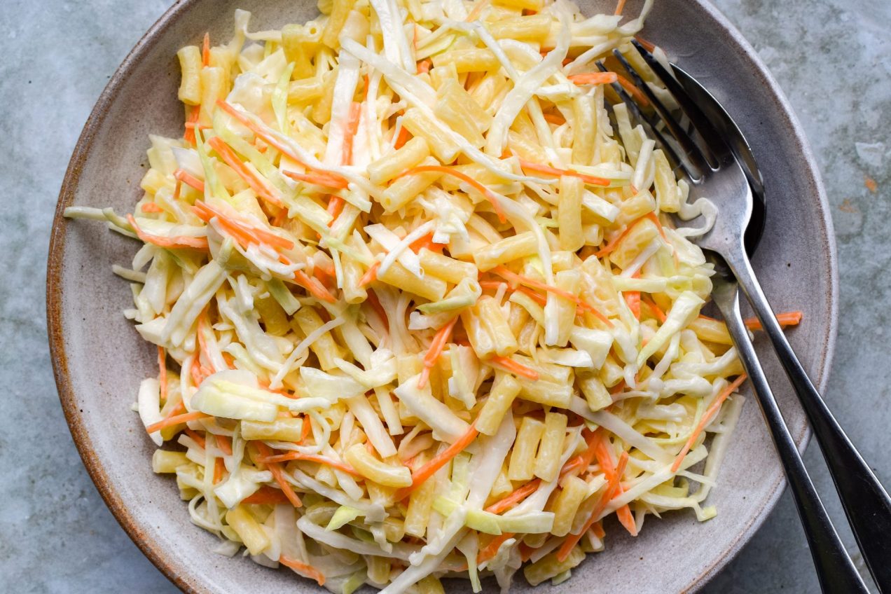 Pasta slaw piled into a stone bowl on a green background.