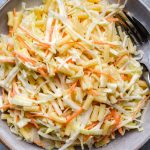 Pasta slaw piled into a stone bowl on a green background.