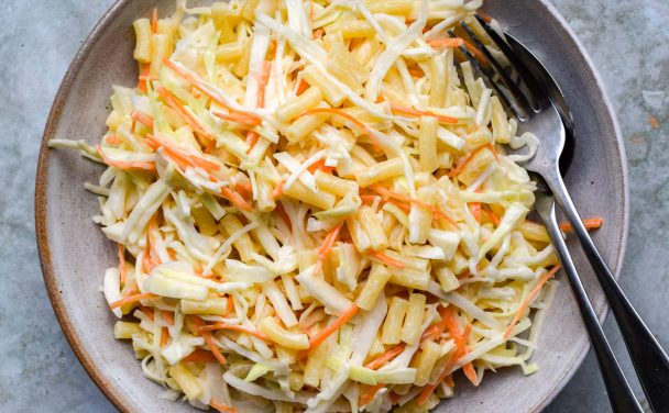 Pasta slaw piled into a stone bowl on a green background.