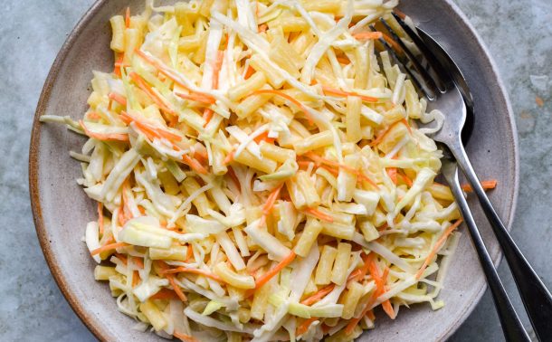 Pasta slaw piled into a stone bowl on a green background.