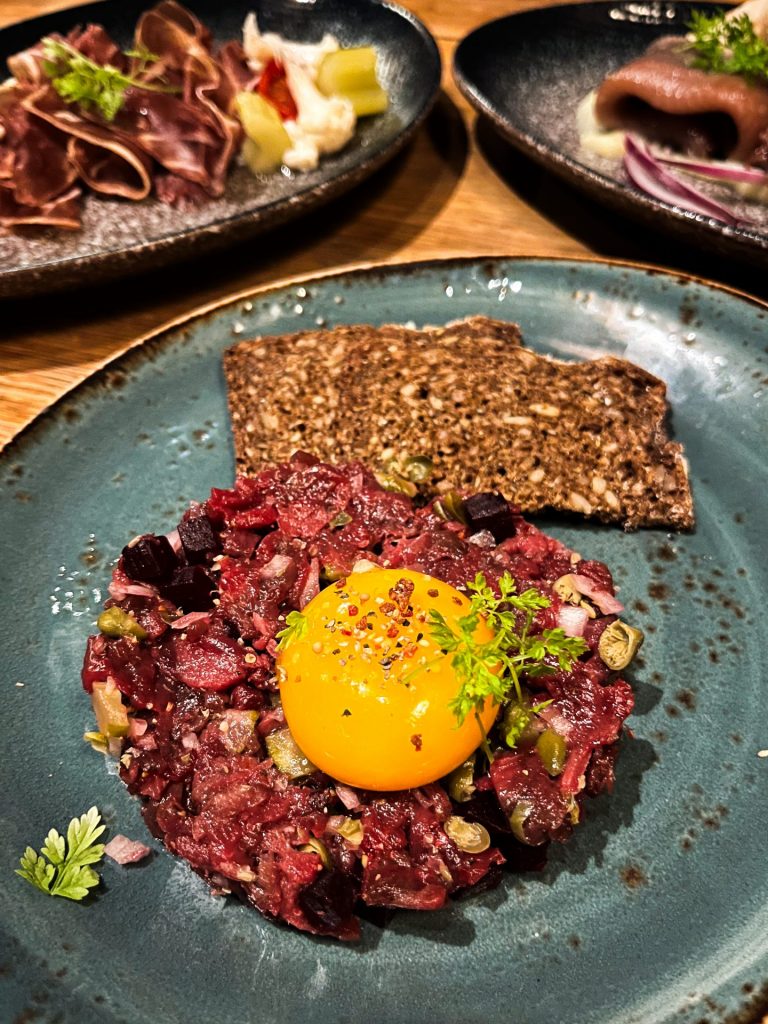 Reindeer tartare topped with an egg yolk with brown bread on a blue plate.