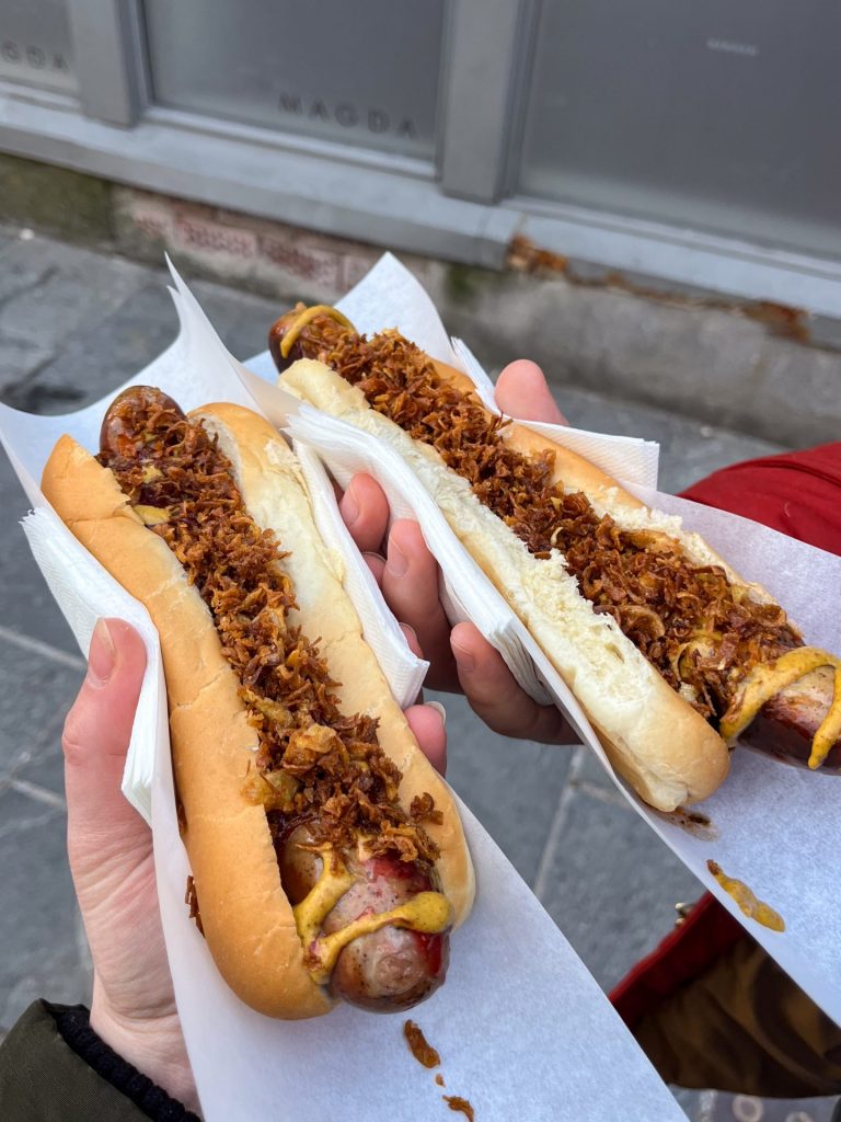 Hands holding a pair of hot dogs with crispy onions and traditional Norwegian sauces.