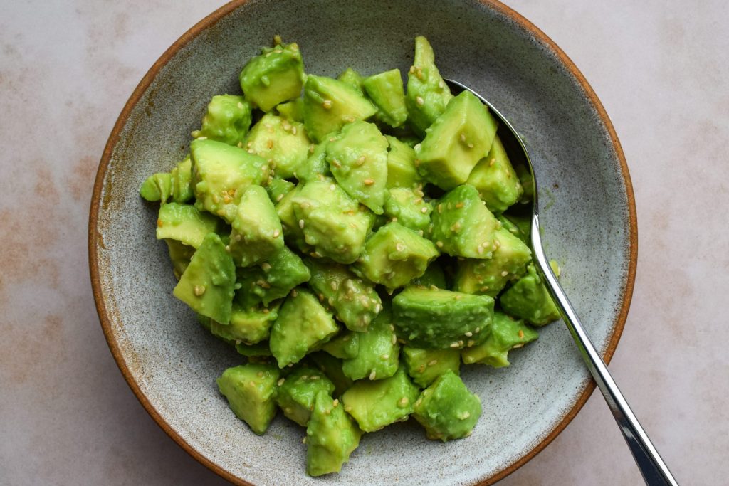 Bowl of diced avocado tossed with sesame seeds and seasonings.