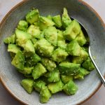 Bowl of diced avocado tossed with sesame seeds and seasonings.