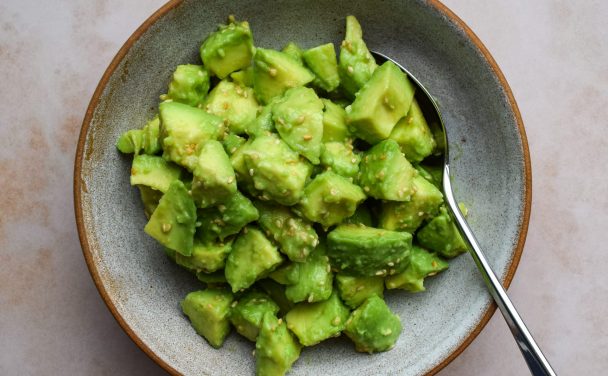 Bowl of diced avocado tossed with sesame seeds and seasonings.