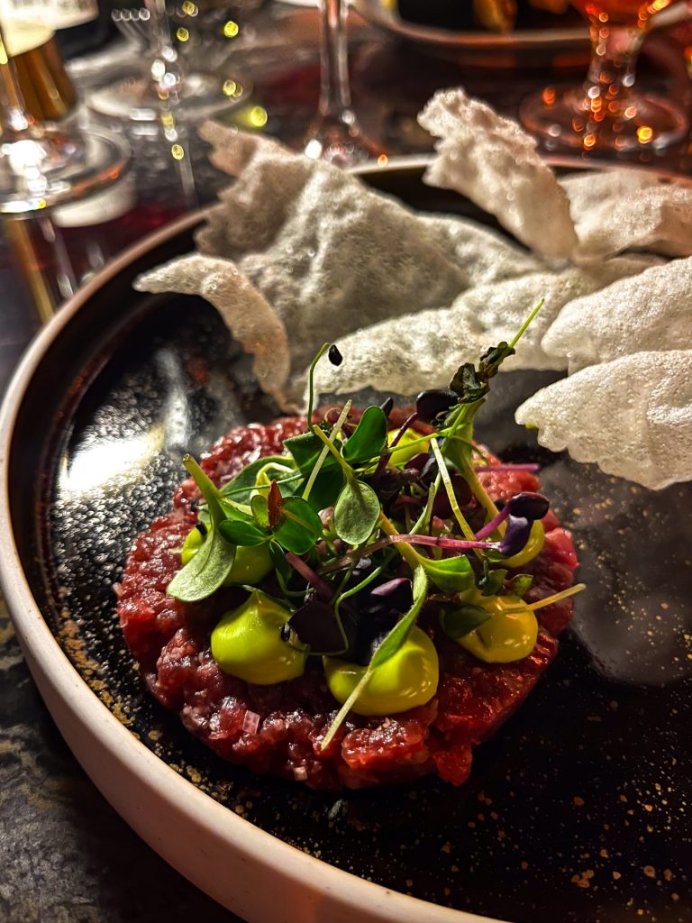 Steak tartare on a black plate with beef crisps in the background.