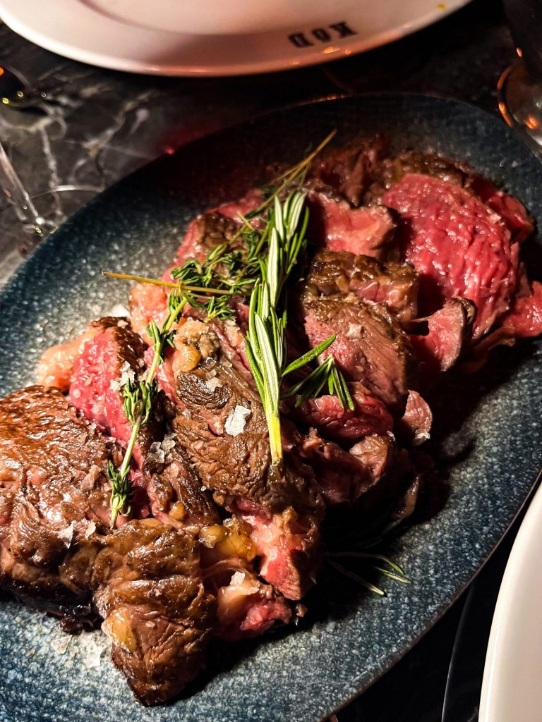 Sliced medium rare rib eye topped with fresh herbs.