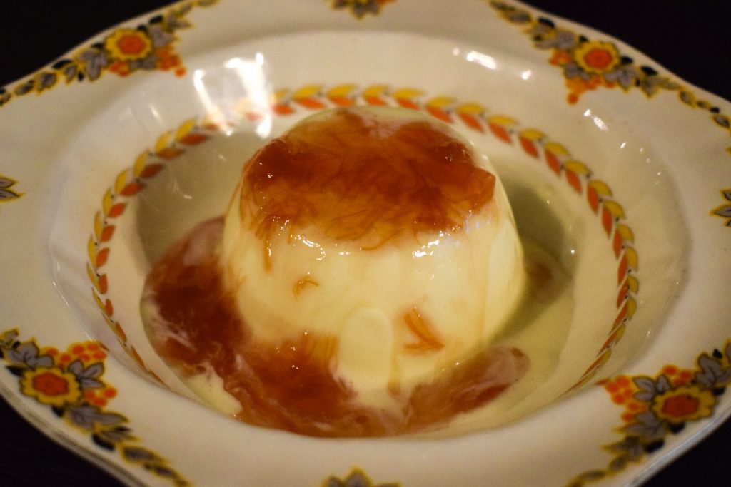 Buttermilk Bavarois on a pattered plate topped with rhubarb compote.