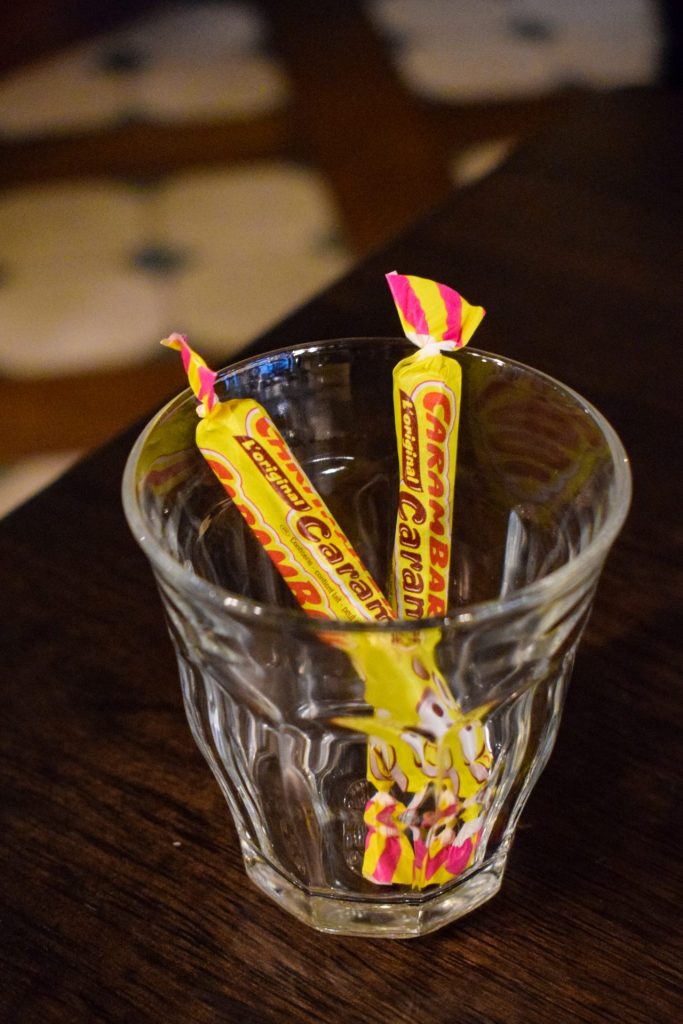 Glass with two carambar in yellow and pink wrappers on a pub table.