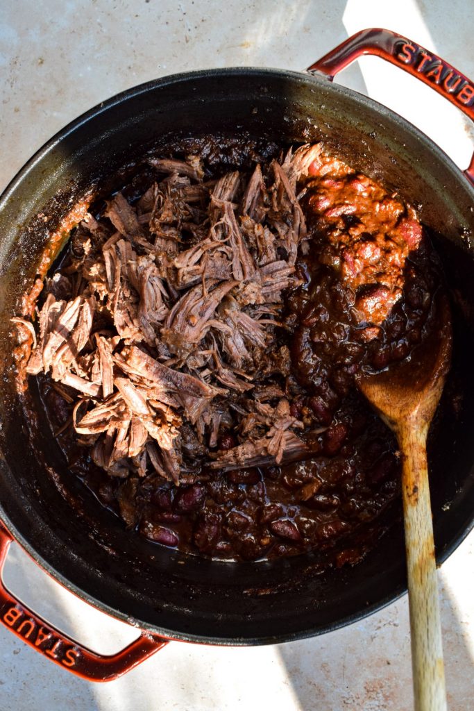 Shredded slow cooked beef on top of a pot of chili with a wooden spoon.