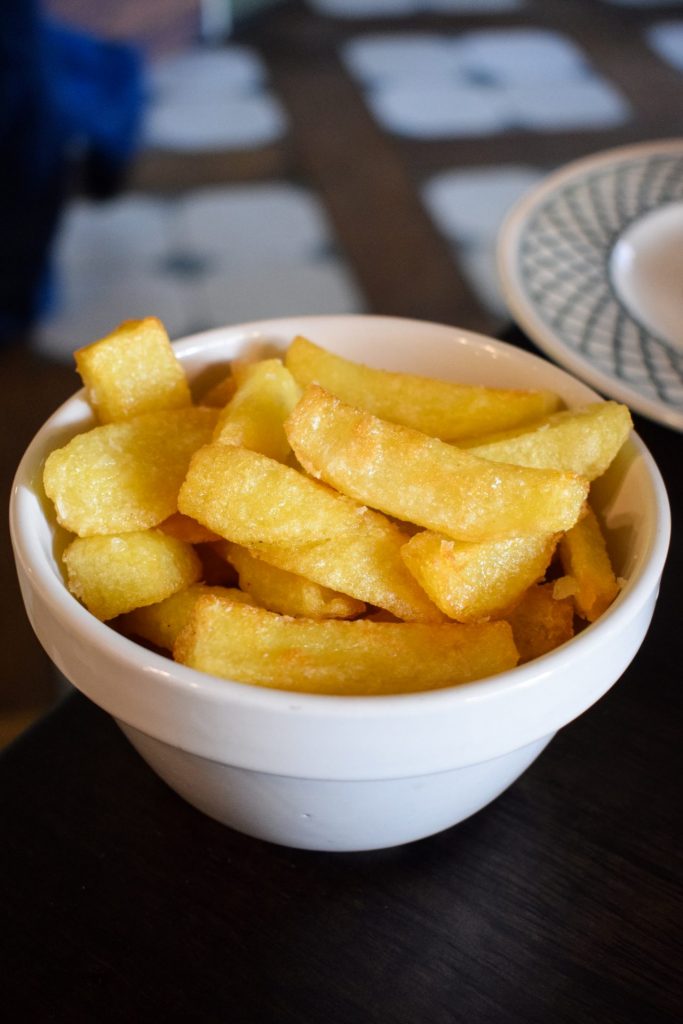 White pudding bowl of chips on a pub table.