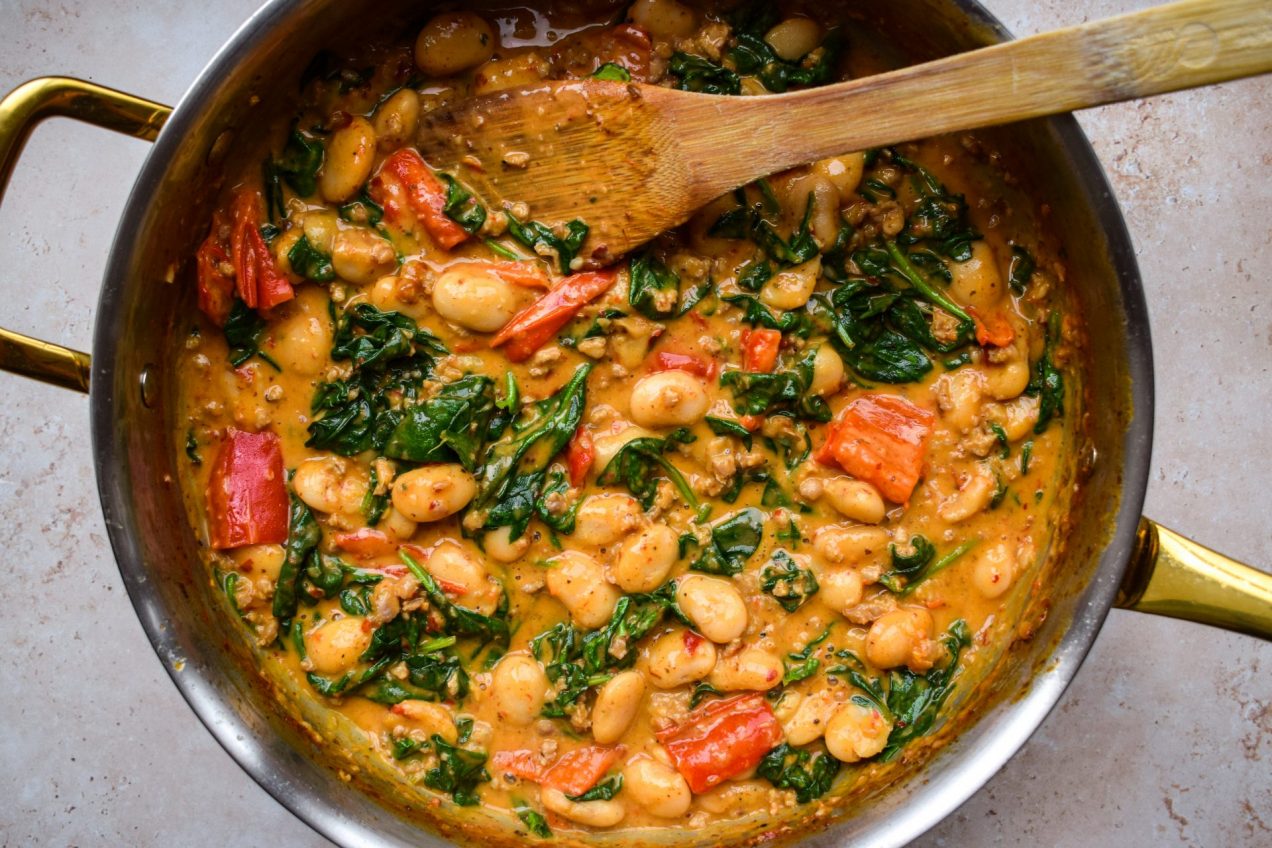 Close up of a pan of creamy butter beans, spinach and red peppers.