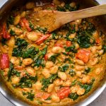 Close up of a pan of creamy butter beans, spinach and red peppers.