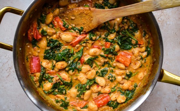 Close up of a pan of creamy butter beans, spinach and red peppers.
