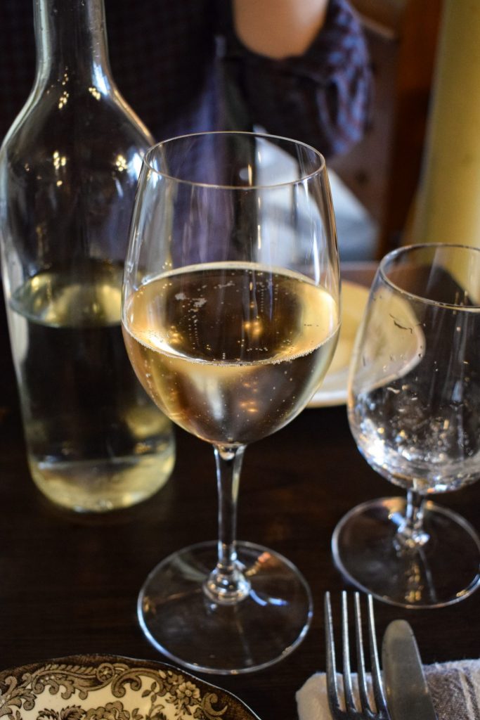 Glass of Cremant on a table with other glasses and a bottle of water.