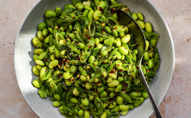 Edamame and sliced sugar snap pea salad with dried chilli flakes in a grey bowl.