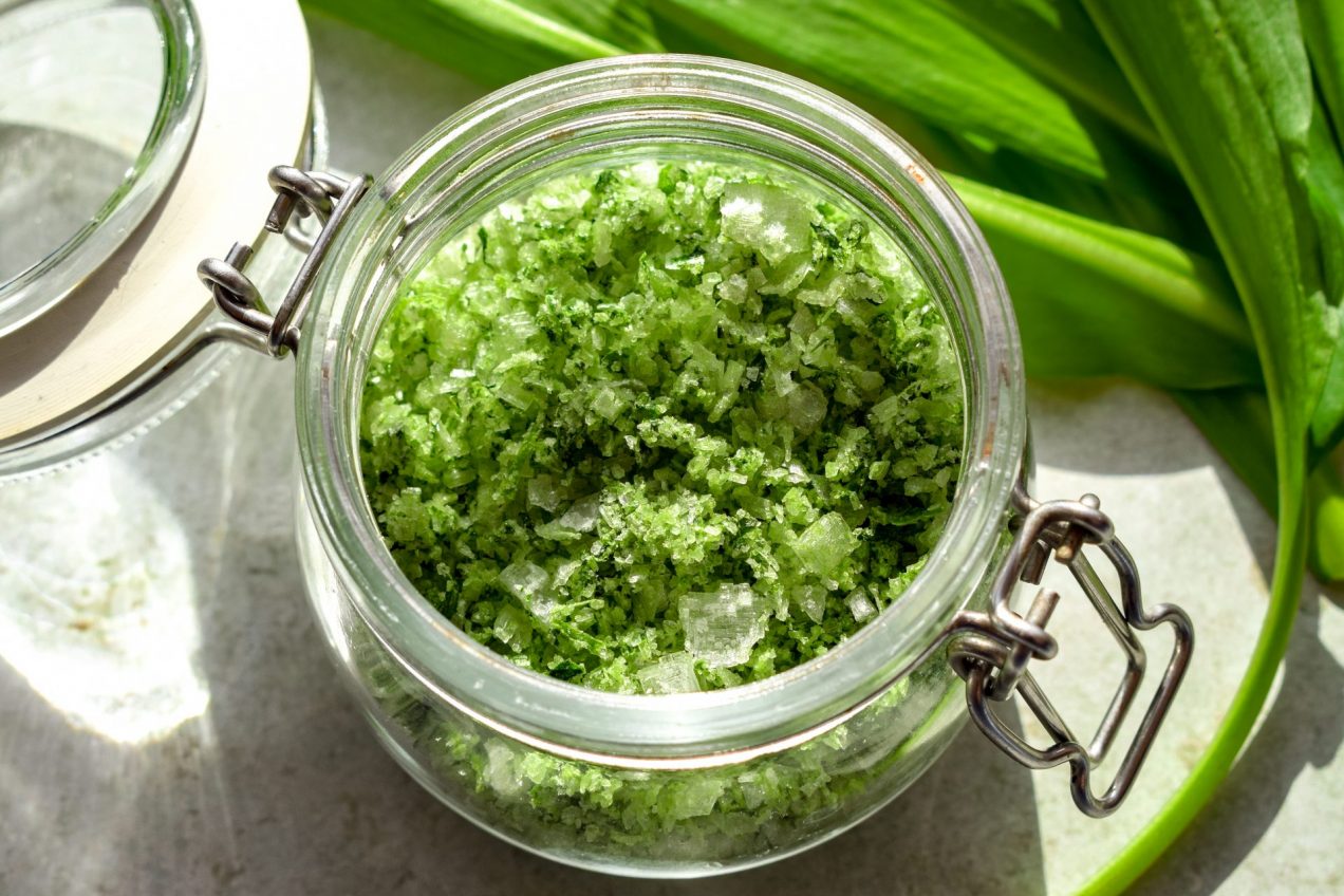 Close up of a small clip-top jar of wild garlic salt, with wild garlic leaves off to one side.