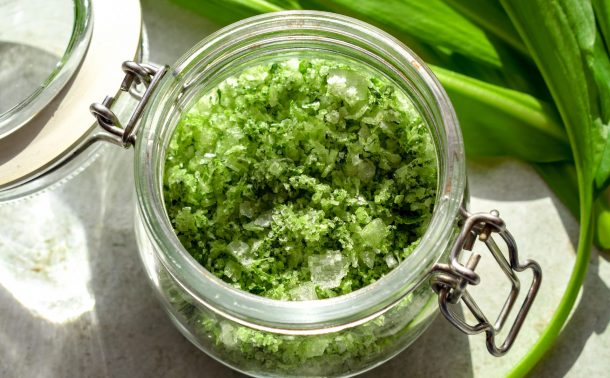 Close up of a small clip-top jar of wild garlic salt, with wild garlic leaves off to one side.