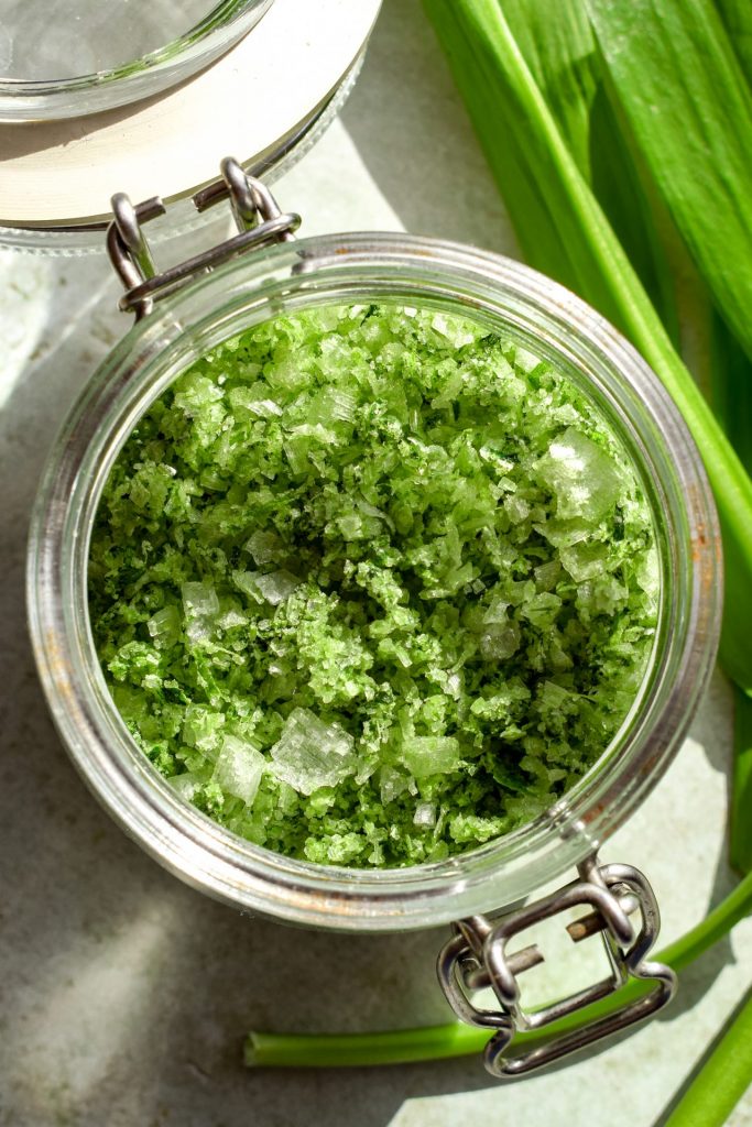 Overhead shot of wild garlic salt in a small clip top jar, next to a few fresh wild garlic leaves.