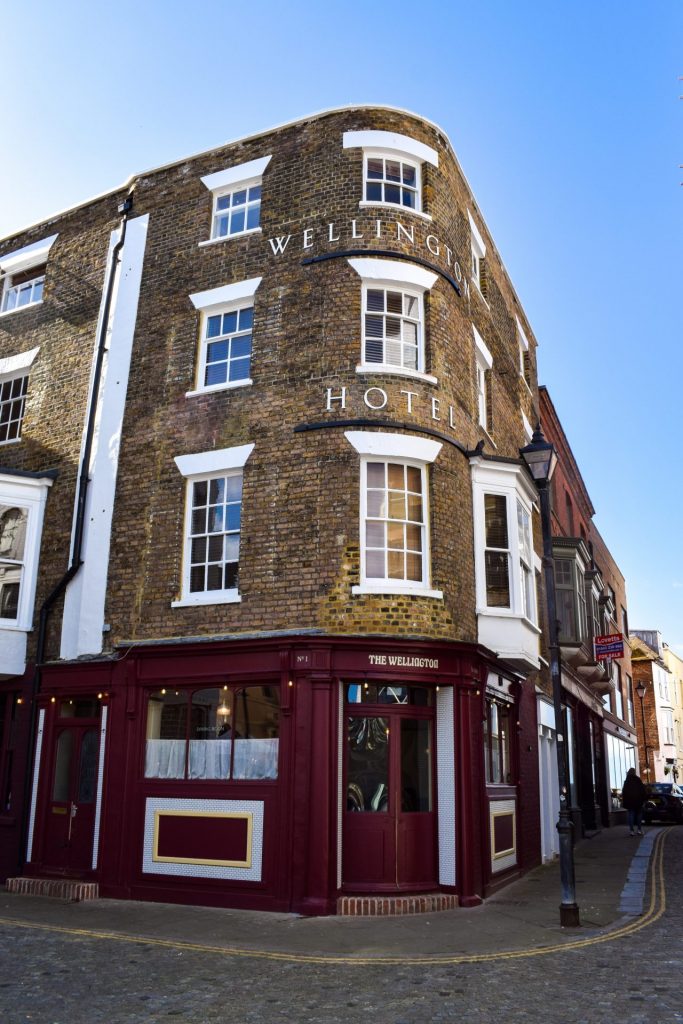 Outside facade of The Wellington in Margate painted dark read with plain brickwork on the top three floors.