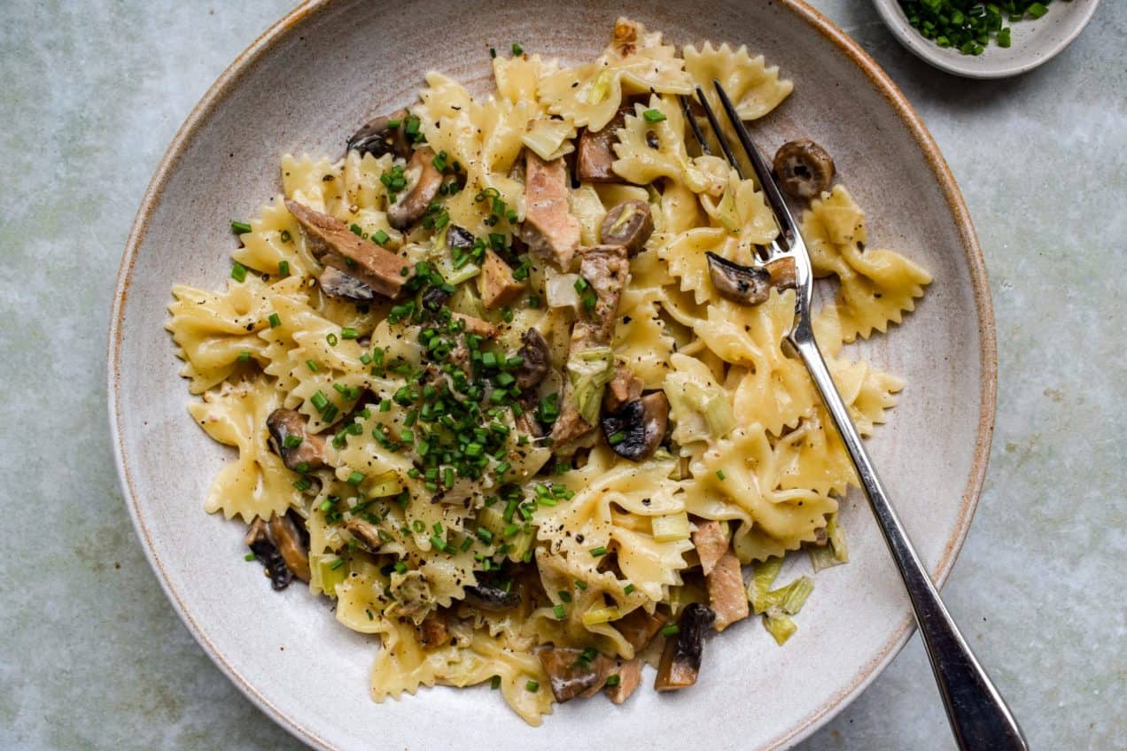Stone bowl of pasta bows with roast pork, mushrooms and leeks, with snipped chives scattered on top.