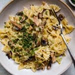 Stone bowl of pasta bows with roast pork, mushrooms and leeks, with snipped chives scattered on top.