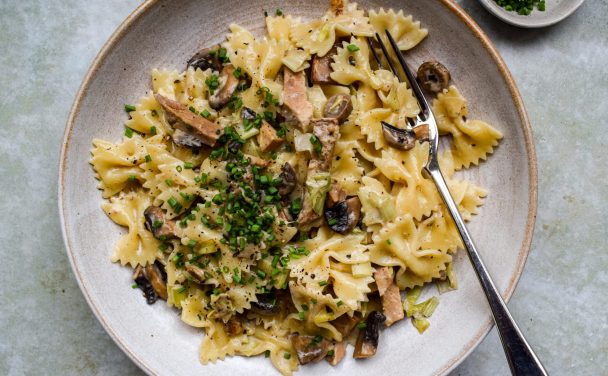 Stone bowl of pasta bows with roast pork, mushrooms and leeks, with snipped chives scattered on top.