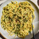 Overhead image of a bowl of caper, lemon, garlic and chilli spaghetti in direct sunlight.