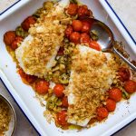 Blue and white baking tray of fish fillet and roasted tomatoes topped with breadcrumbs.
