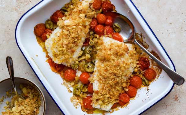 Blue and white baking tray of fish fillet and roasted tomatoes topped with breadcrumbs.