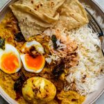 Bowl of egg curry, rice and roti close up. One of the eggs is cut in half to show the soft middle.