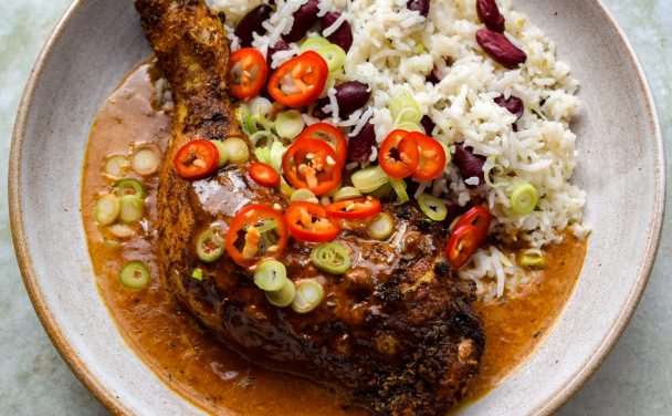 Jerk chicken leg in cream sauce with red beans and rice. Chopped spring onions and chillies are scattered on top.