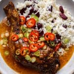 Close up of jerk chicken with a cream gravy, red beans and rice, topped with sliced chillies and spring onions.