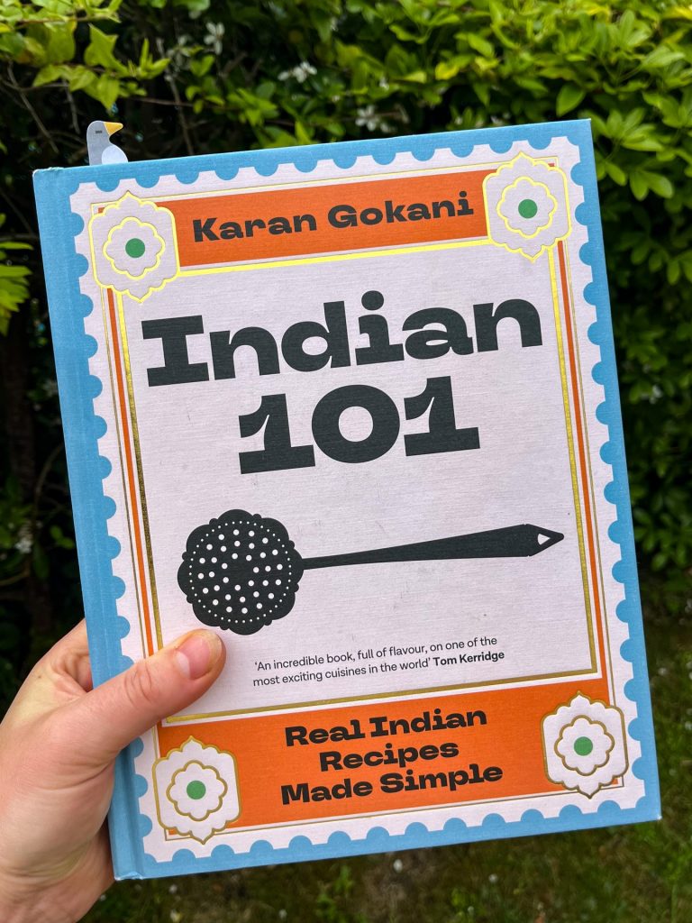 Hand holding up a copy of Indian 101 cookbook.
