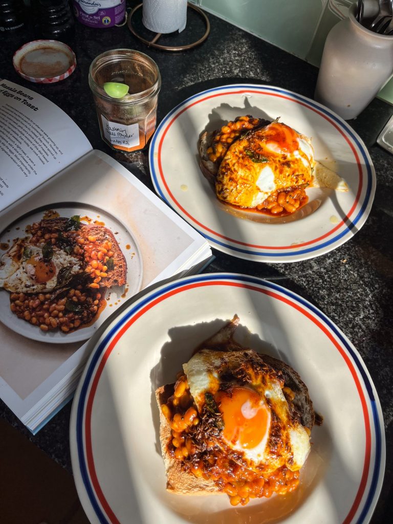 Two plates of masala beans topped with fried eggs next to an open cookbook.