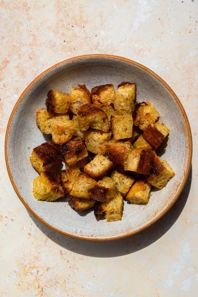 Stone bowl of homemade croutons pictured overhead in direct sunlight.