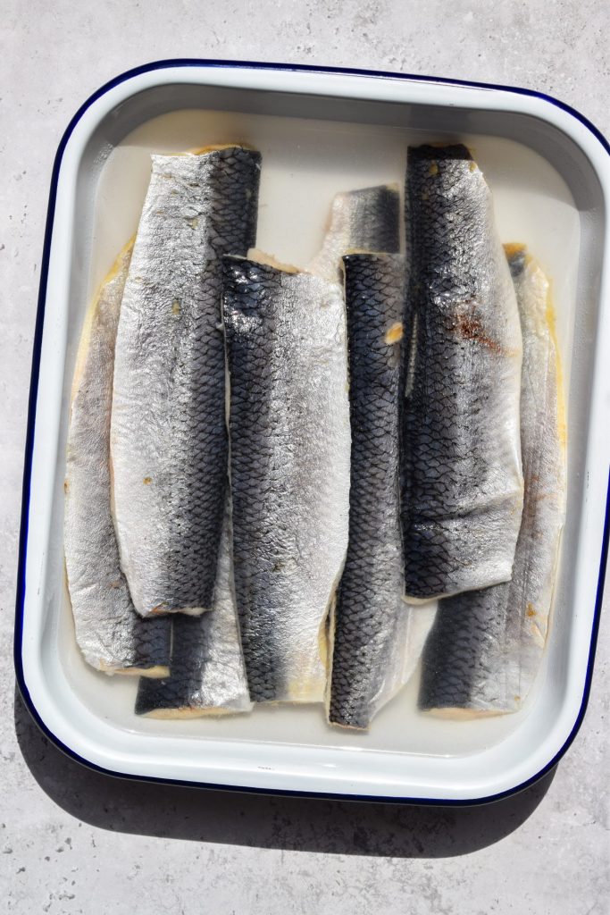 Tray of herring fillets marinating in brine.